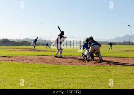 Verschiedene Baseballspielerinnen in Aktion auf sonnigem Baseballfeld während des Spiels Stockfoto