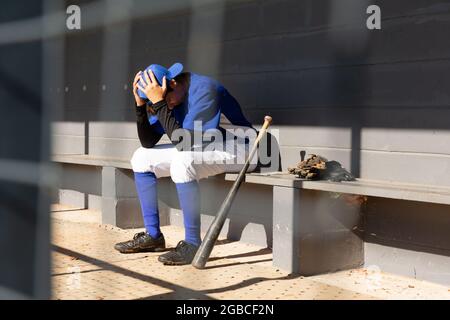 Mixed-Race-Baseballspielerin sitzt während des Spiels auf der Bank mit Kopf in den Händen Stockfoto