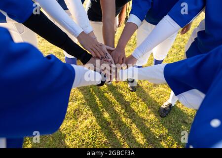 Eine vielfältige Gruppe weiblicher Baseballspieler, die auf dem sonnigen Baseballfeld einen Handstapel bilden Stockfoto