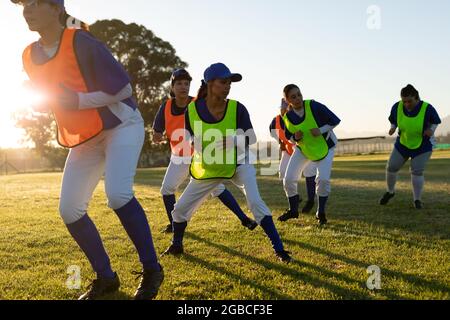 Verschiedene Baseballspielerinnen in bunten Lätzchen trainieren bei Sonnenaufgang auf dem Spielfeld Stockfoto