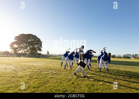 Verschiedene Baseballspielerinnen mit Trainer, die sich im Feld von der Hüfte aus aufwärmen Stockfoto