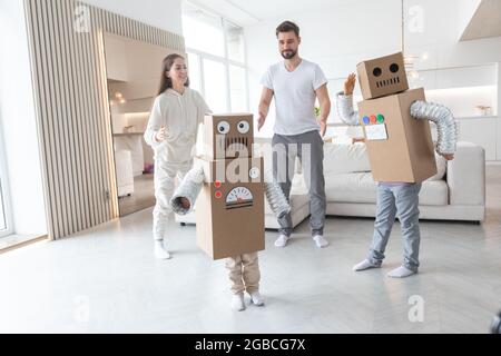 Fröhliche Familie von Eltern und zwei Kindern, die zu Hause tanzen wie Roboter, Kinder tragen handgefertigte Moving-Box-Kostüme aus Pappe Stockfoto