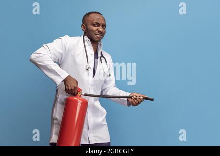 Porträt eines jungen Mannes, Arztes, therapeutischen oder medizinischen Beraters mit Feuerlöscher isoliert auf blauem Hintergrund. Lustige Meme Emotionen. Stockfoto