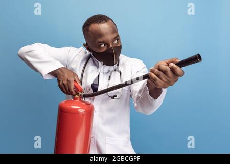 Porträt eines jungen Mannes, Arztes, therapeutischen oder medizinischen Beraters mit Feuerlöscher isoliert auf blauem Hintergrund. Lustige Meme Emotionen. Stockfoto