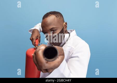 Porträt eines jungen Mannes, Arztes, therapeutischen oder medizinischen Beraters mit Feuerlöscher isoliert auf blauem Hintergrund. Lustige Meme Emotionen. Stockfoto