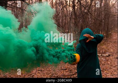 Eine gruselige Hexe hält einen dampfenden Kürbis in einen tiefen Wald. Jack o Laterne mit grünem Rauch für halloween Stockfoto