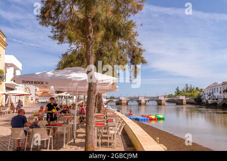 Riverside Cafe Restaurant am Fluss Gilao Tavira. Im Hintergrund ist die römische Brücke oder Ponte Romana de Tavira zu sehen. Tavira East Alga Stockfoto