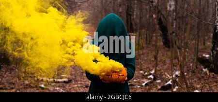 Eine gruselige Hexe hält einen dampfenden Kürbis in einen tiefen Wald. Jack o Laterne strahlt für halloween gelben Rauch aus Stockfoto