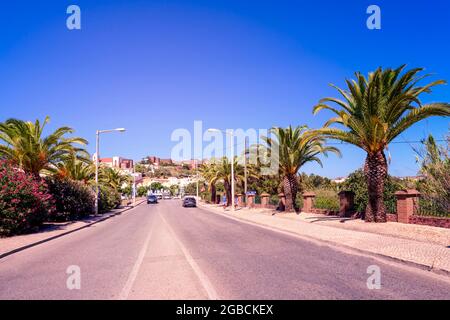 Die Hauptstraße nach Silves, gesäumt von Palmen, über eine Brücke über den Fluss Arade. Das Schloss Silves ist auf der Skyline zu sehen Stockfoto