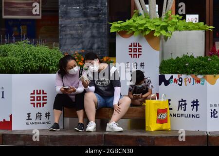 Peking, China. August 2021. Touristen tragen Gesichtsmasken als Vorsichtsmaßnahme gegen die Verbreitung von Covid-19, die sie sitzend sehen, während sie ihre Smartphones in der Wangfujing Commercial Street in Peking benutzen. (Foto von Sheldon Cooper/SOPA Images/Sipa USA) Quelle: SIPA USA/Alamy Live News Stockfoto