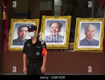 Peking, China. August 2021. Ein Sicherheitsbeamter, der als Vorsichtsmaßnahme gegen die Verbreitung von covid-19 eine Gesichtsmaske trägt, geht an den Porträts von Mao Zedong vorbei, die im Fenster des Pekinger Fotostudios in der Handelsstraße Wangfujing in Peking aufgestellt wurden. (Foto von Sheldon Cooper/SOPA Images/Sipa USA) Quelle: SIPA USA/Alamy Live News Stockfoto