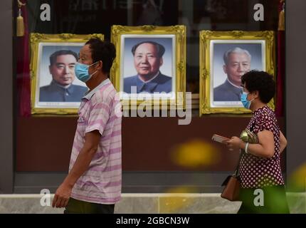 Peking, China. August 2021. Ein paar Touristen, die Gesichtsmasken tragen, als Vorsichtsmaßnahme gegen die Verbreitung von covid-19, gehen an den Porträts von Mao Zedong vorbei, die im Fenster des Pekinger Fotostudios in der Wangfujing Commercial Street aufgestellt wurden. (Foto von Sheldon Cooper/SOPA Images/Sipa USA) Quelle: SIPA USA/Alamy Live News Stockfoto