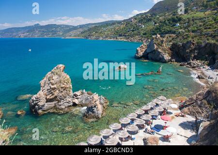 Cefalù, Palermo, Sizilien, Italien. Blick über das klare türkisfarbene Wasser der Calura Bay, Touristen entspannen sich unter Sonnenschirmen am Strand. Stockfoto