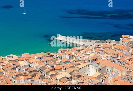 Cefalù, Palermo, Sizilien, Italien. Blick über die Ziegeldächer der Altstadt von La Rocca, das türkisfarbene Wasser des Tyrrhenischen Meeres dahinter. Stockfoto