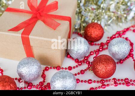 Weihnachtsgeschenk und Dekorationen für das neue Jahr. Weihnachtliche Komposition aus silbernen und roten Kugeln, Geschenkbox, Perlen und Glitzergirlande auf weißem Hintergrund. Stockfoto