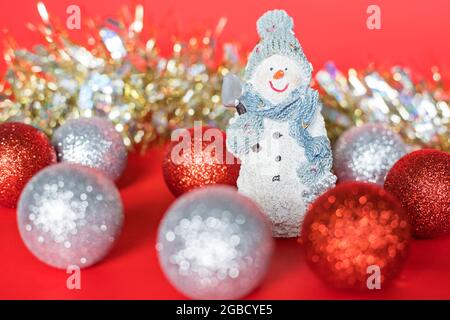 Weihnachten und Neujahr Baumdekorationen. Weihnachtliche Komposition aus kleinem Schneemann, Silber und Kugeln und Glitzergirlande auf rotem Hintergrund. Stockfoto