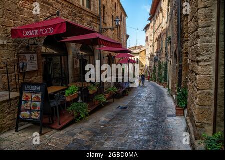 Volterra, Toskana, Italien. August 2020. Eine Gasse des historischen Dorfes, gekennzeichnet durch die Steinstraße, gehen Touristen durch die Restaurants. Stockfoto