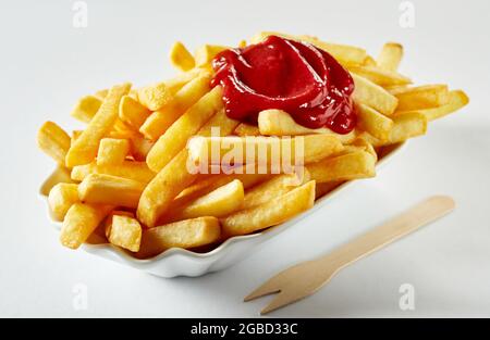 Appetitliche Pommes frites mit Ketchup in einer Keramikschale in der Nähe eines umweltfreundlichen Stickstisches auf weißem Hintergrund Stockfoto