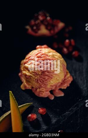 Von oben mit schmackhaftem, glattem Gelato zwischen reifen Mangoscheiben und saftigen Granatapfelkernen auf verschwommenem Hintergrund Stockfoto