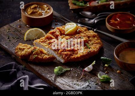 Von oben leckeres gebratenes Hühnchen-Schnitzel auf Schneidebrett mit verschütteten Gewürzen und Saucen in Schüsseln Stockfoto