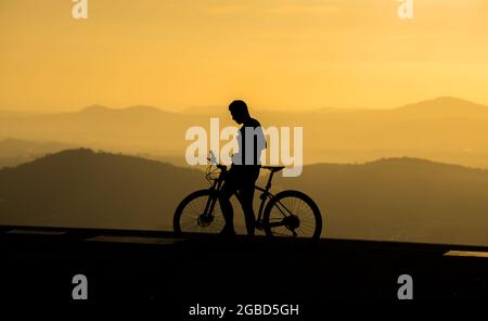 Silhouette eines Radfahrers bei Sonnenuntergang und Bergschichten als Hintergrund Stockfoto