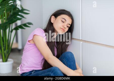 Porträt eines indischen Teenagers, das in der Nähe der Wand sitzt und sich zu Hause unglücklich und deprimiert fühlt Stockfoto