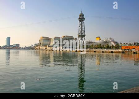 Blick über den Hafen zum Kreuzfahrtterminal mit angedockten Schiffen, dem Seilbahnturm und Reflexionen im Mittelmeer, Barcelona, Spanien. Stockfoto