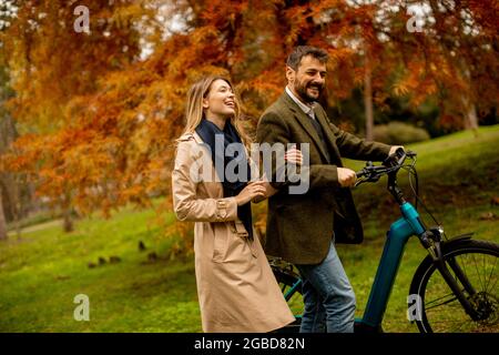 Schönes junges Paar im Herbstpark mit Elektrofahrrad Stockfoto