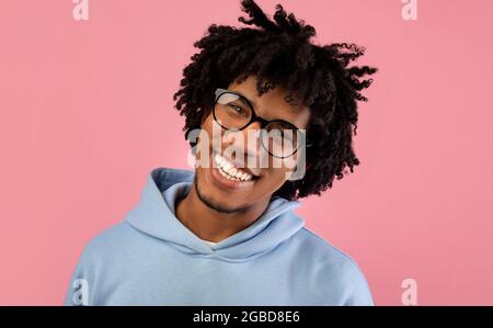 Porträt eines positiven jungen Teenagers mit einem attraktiven Lächeln, das eine Brille trägt und die Kamera auf einem rosa Hintergrund im Studio anschaut Stockfoto