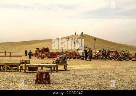 Yazd, Desert, Iran, 20. Februar 2021: Junge Menschen steigen abwechselnd in ATVs ein, während Kinder und Erwachsene auf den Sanddünen spielen. Stockfoto