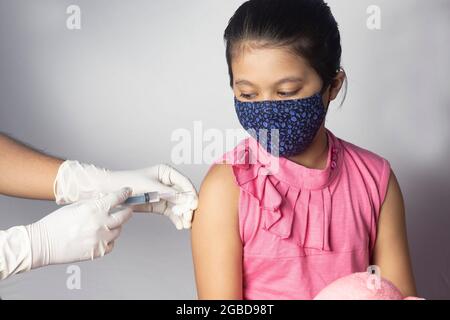 Ein indisches Mädchen, das in einer Nasenmaske eine Impfdosis auf weißem Hintergrund erhält Stockfoto