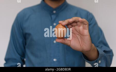 Männliche Hand hält Ostern braun Huhn Ei isoliert auf grauem Hintergrund Stockfoto