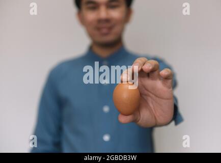 Männliche Hand hält Ostern braun Huhn Ei isoliert auf grauem Hintergrund Stockfoto