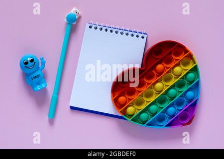 Zurück zum Schulkonzept.Notizblatt, blauer Stift und Antistress-Spielzeug in Form eines Herzens auf einem rosa Hintergrund. Blick von oben..Flat Lay Stockfoto