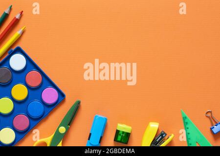 Zurück zum Schulkonzept. Schulbedarf und Bürobedarf auf dem Bürotisch. Orangefarbener Hintergrund.flache Verlegung Stockfoto
