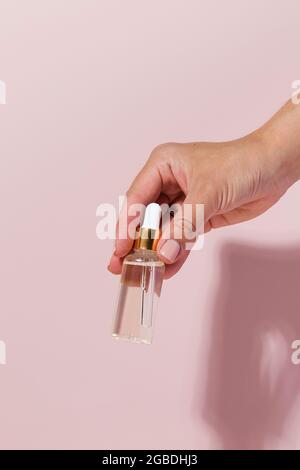 Ein Nachbau einer Glasflasche mit einem Serum oder Öl für die Haut in der Hand auf einem rosa Hintergrund. Stockfoto