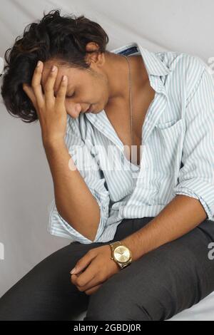 Vertikale Aufnahme eines jungen indischen Mannes, der mit einem depressiven Gesicht sitzt Stockfoto
