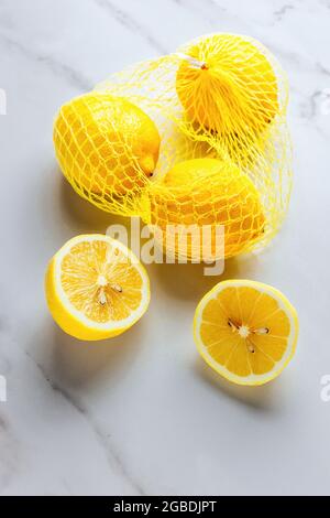 Frische Zitronen auf weißem Marmorhintergrund mit ganzen Zitronen, halben Zitronen und Zitronen in Netzverpackung - TEXTERRAUM, FOODPIX WEISS Stockfoto