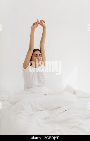 Attraktive junge Frau, die im Bett aufwacht und ihre Arme streckt. Stockfoto