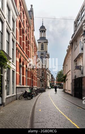 Breda, Niederlande 28. Juni 2021. Eine Straße im Stadtzentrum mit alten historischen Gebäuden, Geschäften, einem Bürgersteig, einer Kirche und einer Person, auf der man Rad fahren kann Stockfoto