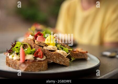 Gesundes hausgemachtes Club Sandwich mit frischen Zutaten wie Tomaten, Salat, Salat, Speck, Blumenkohl und Huhn auf Scheiben rustikalen braunen Brotes b Stockfoto