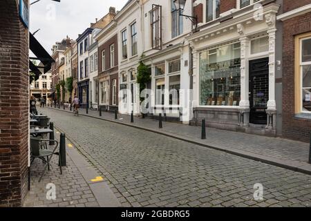 Breda, Niederlande 28. Juni 2021. Straße im Stadtzentrum mit alten historischen Gebäuden, einem Bürgersteig, Geschäften, Häusern und einem Radfahrer auf einer sonnigen da Stockfoto