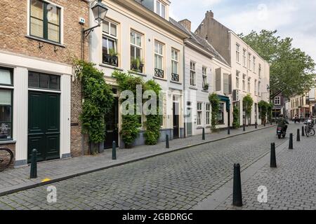 Breda, Niederlande 28. Juni 2021. Straße im Stadtzentrum mit alten historischen Gebäuden, einem Bürgersteig, Geschäften, Häusern und einem Motorroller-Fahrer auf einem Su Stockfoto