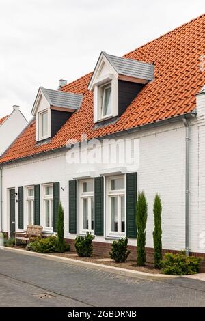 Weiße, moderne Häuser mit orangefarbenem Dach in Thorn, Limburg, Niederlande, einem Dorf, das für seine weißen Häuser und Gebäude bekannt ist. Grüne Fensterläden nebenan Stockfoto