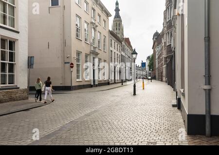 Breda, Niederlande 28. Juni 2021. Straße im Stadtzentrum mit alten historischen Gebäuden mit hellen Fassaden, einem Bürgersteig, einer Kirche und Menschen Wal Stockfoto