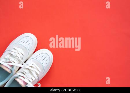 Weiße Sneakers isoliert auf rotem Hintergrund mit Kopierraum. Draufsicht. Flach liegend. Sportbekleidung. Damenschuhe. Stockfoto