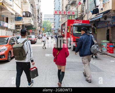 HONGKONG, HONGKONG - 24. Jul 2018: Drei Personen ohne Beziehung, die auf einer Straße in Hongkong von der Kamera weggehen...Sie trägt ein knallrotes, kurzes Kleid...L Stockfoto