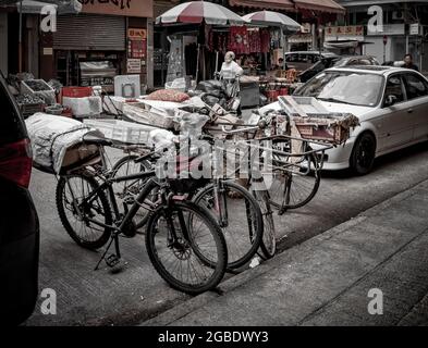 HONGKONG, HONGKONG - 24. Jul 2018: Eine Gruppe von Lieferfahrrädern parkte an der Bordsteinkante zwischen Autos auf einer Straße in Hongkong... Stockfoto