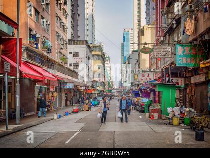 HONGKONG, HONGKONG - 24. Jul 2018: Zwei Menschen, die mit ihren Geschäften eine alte HK-Straße entlang gehen... vorbei an roten Markisen, grünen Ständen und mehr. Stockfoto