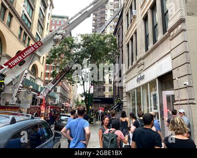 New York, NY, USA - 3. Aug 2021: Menschen, die auf dem Bürgersteig aussteigen, als Rettungskräfte das Feuer in einem nahe gelegenen Gebäude löschen Stockfoto